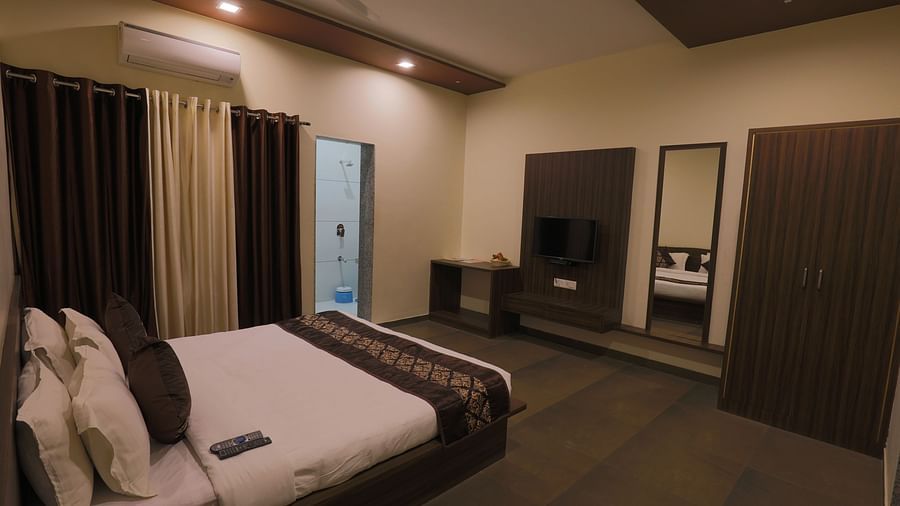 A comfortable bedroom with a double bed, dark furniture, and soft lighting - Vishal Lords Inn Gir Forest