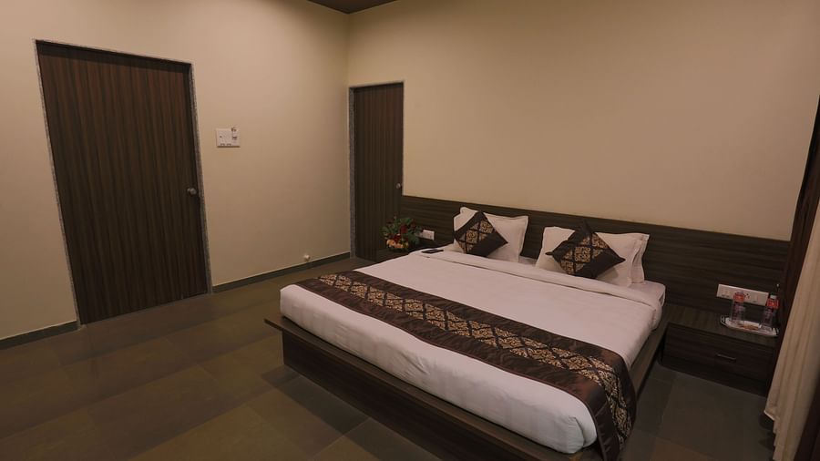 A bedroom with a double bed, dark wooden furniture, and a closed door - Vishal Lords Inn Gir Forest