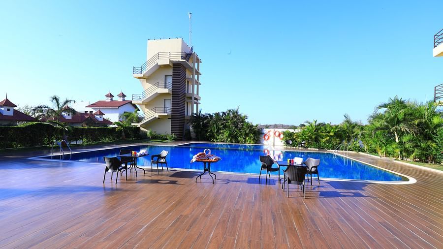 A large swimming pool with sun loungers and umbrellas, surrounded by greenery - Vishal Lords Inn Gir Forest