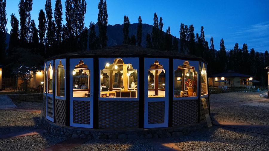 The exterior of a building with large windows, glowing warmly against a dark, tree-lined background at night at White Sands Resort, Ladakh.