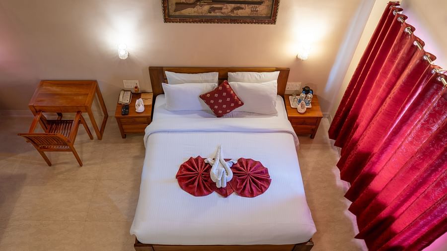 A top-down view of Attic Villa shows a simple king size bed with red accents and clean white linens | Woodstock Resorts, Coorg