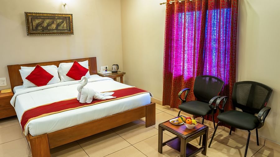 Attic Villa equipped with a king size bed, bedside tables, and chairs, accented with red curtains | Woodstock Resorts, Coorg