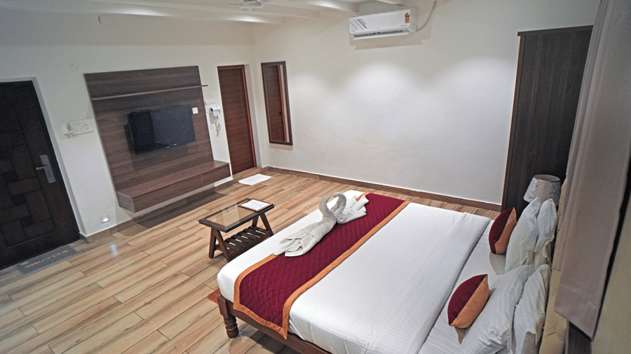 A room at WOW Naturefull Resorts, Yercaud, with a large bed, spreads, pillows, an air-conditioner, a table, and a mirror.