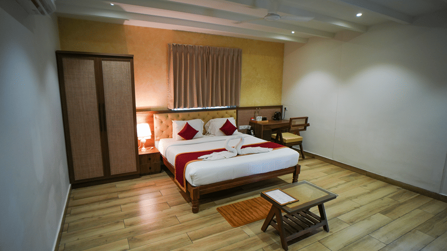 A room at WOW Naturefull Resorts, Yercaud, with a large bed, spreads, pillows, an air-conditioner, a table, and a mirror.