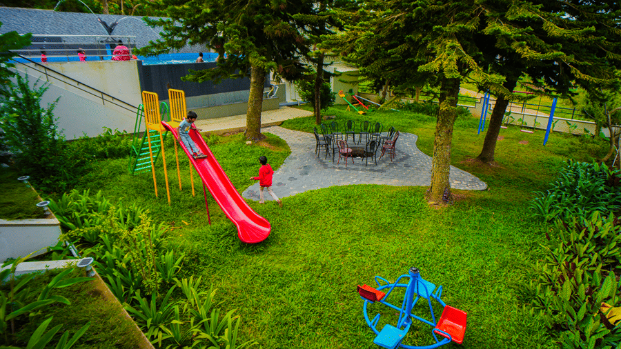 • An overhead view of a playground nestled in a grassy area with trees, featuring a playground slide.