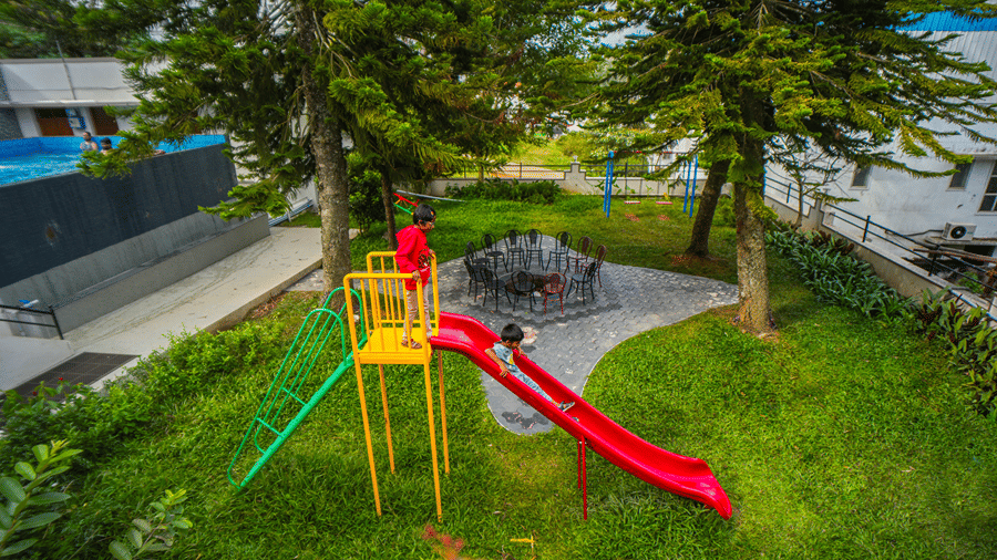 • An overhead view of a playground nestled in a grassy area with trees, featuring a playground slide.