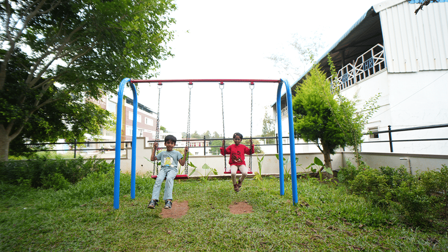 An outdoor play area on a grassy lawn showing children playing on a swing set.