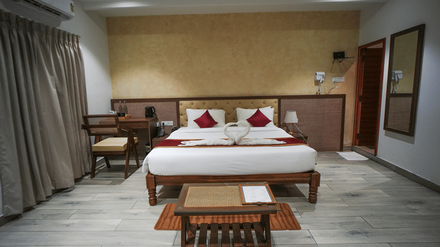 A room at WOW Naturefull Resorts, Yercaud, with a large bed, spreads, pillows, an air-conditioner, a table, and a mirror.