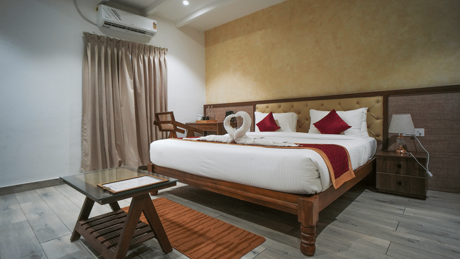 A room at WOW Naturefull Resorts, Yercaud, with a large bed, spreads, pillows, an air-conditioner, a table, and a mirror.