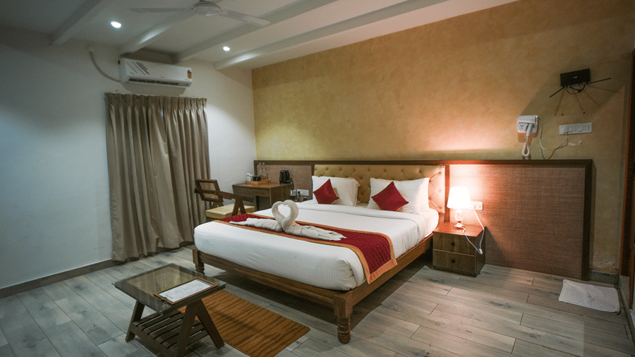 A room at WOW Naturefull Resorts, Yercaud, with a large bed, spreads, pillows, an air-conditioner, a table, and a mirror.