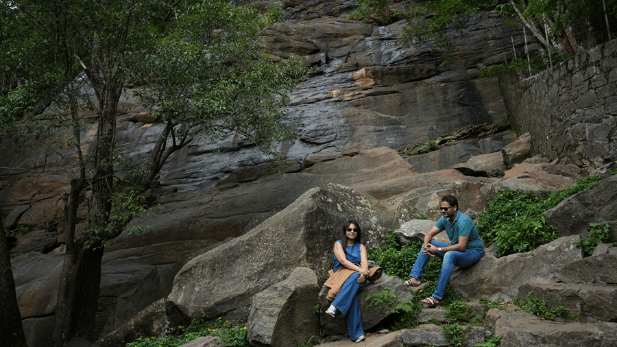 An outdoor rocky landscape surrounded by trees, where people are sitting and resting on large stone boulders.