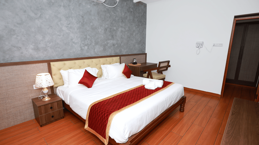 A double bed with a bed side table along with a lamp placed over it at the Standard Room at WOW Naturefull Resorts, Salem.