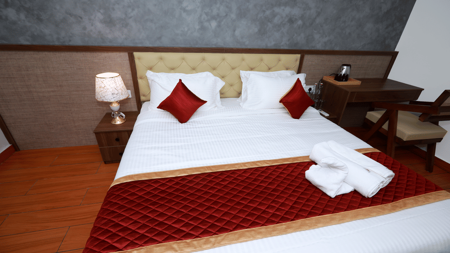 A close-up shot of the double bed at the Standard Room with a maroon bed runner along with white towels kept over it at WOW Naturefull Resorts, Yercaud.