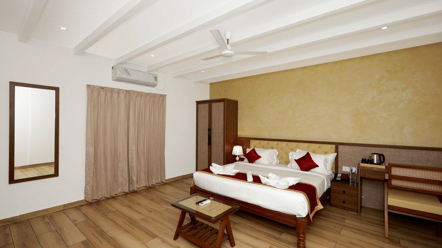 Full-view shot of the Terrace Cottage featuring a double bed, with a wall-mounted split AC above the window covered with beige-coloured curtains at WOW Naturefull Resorts, Yercaud.