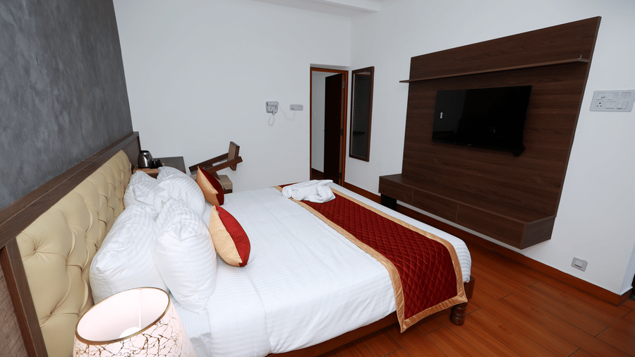 Side view of the double bed kept in the Standard Room of WOW Naturefull Resorts, Yercaud, with a dark grey-coloured wall behind the tufted headboard.