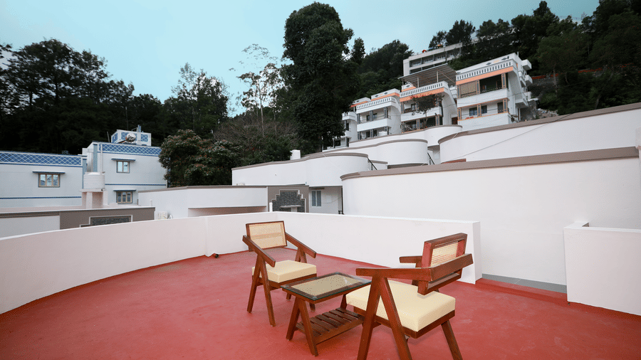 The terrace area with 2 arm chairs and a coffee table with a scenic backdrop of lush green trees and a blue evening sky at WOW Naturefull Resorts, Yercaud.