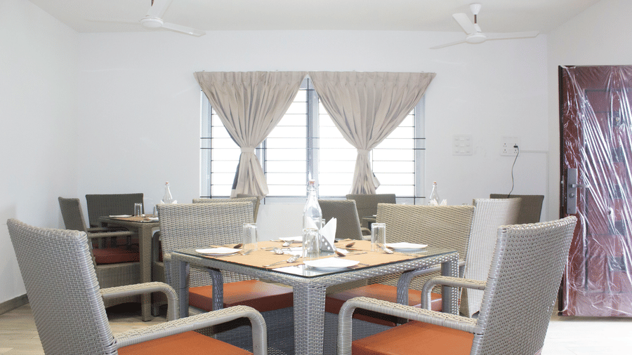 A close-up shot of a well-arranged dining table with 4 chairs kept around it at the Spice and Slice Restaurant at WOW Naturefull Resorts, Yercaud.