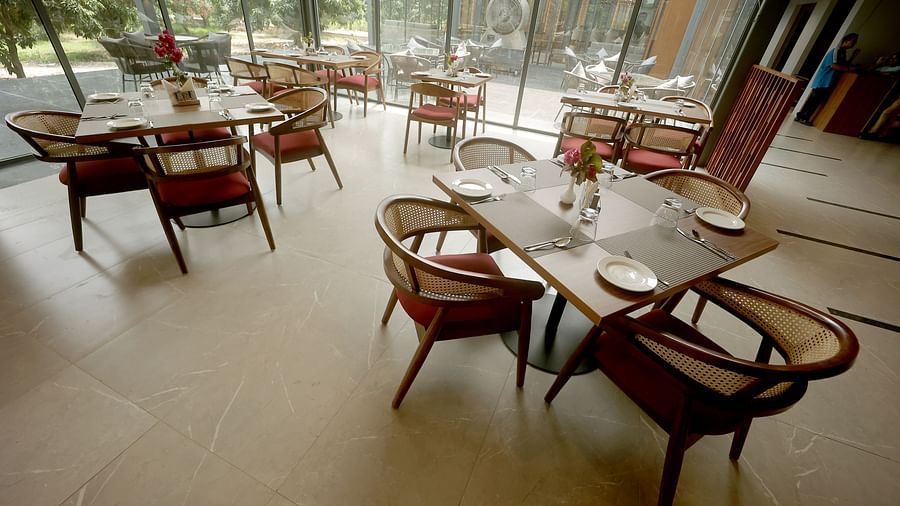 Sunlit dining area with neatly set tables, wooden chairs, and floor-to-ceiling glass windows at Wyndham Garden.
