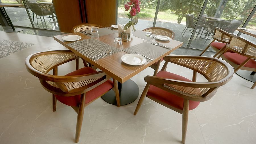 Bright restaurant seating arrangement with wooden chairs and a view of greenery through full-height windows at Wyndham Garden.