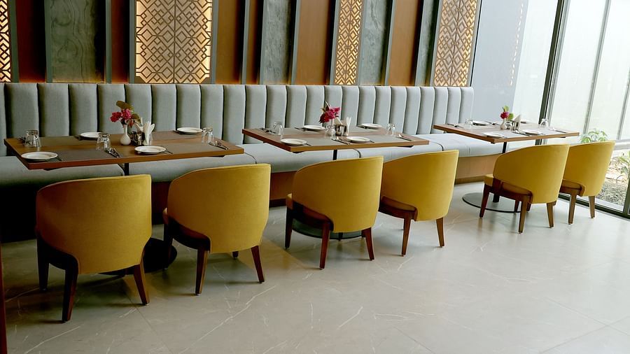 Elegant indoor dining area with mustard yellow chairs and a striped cushioned bench against a decorative wall at Wyndham Garden.