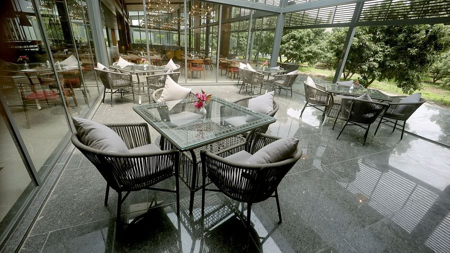 Outdoor dining space with glass walls, grey cushioned chairs, and neatly arranged tables at Wyndham Garden.