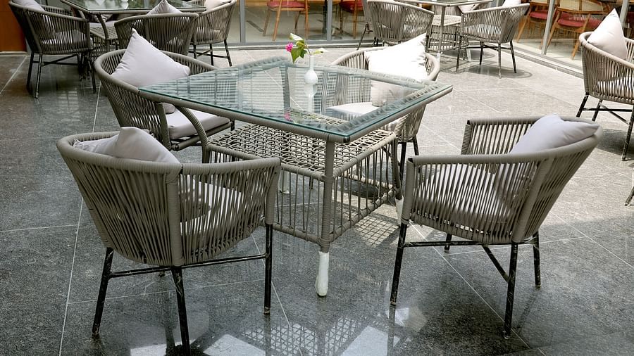 Outdoor dining area with glass-top tables, cushioned wicker chairs, and a single flower vase on each table at Wyndham Garden.