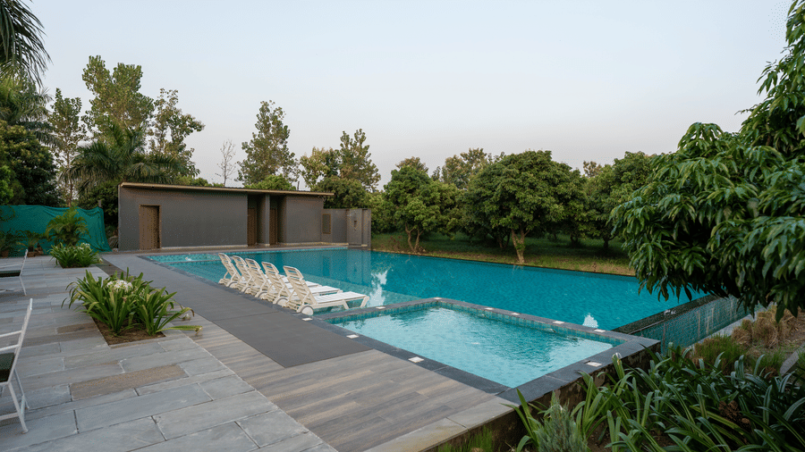 An expansive multi-level outdoor pool area at Wyndham Garden with a smaller square dipping pool leading into the main pool, stone paving, lounge chairs, and surrounded by dense trees.