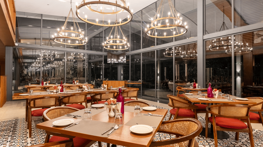 A  stylish restaurant setting at Wyndham Garden with round tables, modern lighting, glass facade interior, dark wood tables, and  circular chandeliers. 