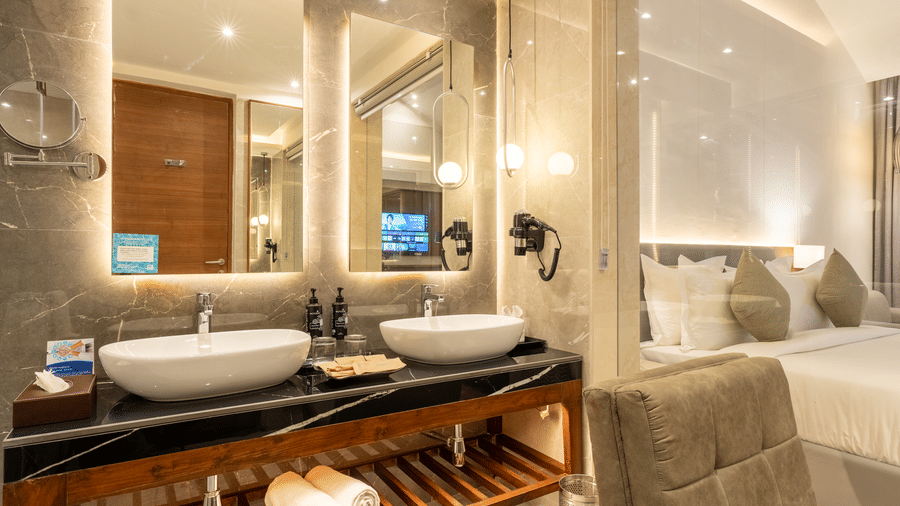 A bathroom at Wyndham Garden with twin vessel sinks on a dark vanity, modern faucets, and large mirrors with built-in lighting.