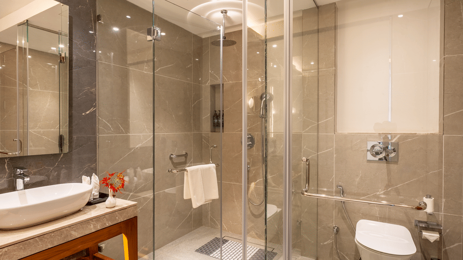 A modern bathroom at Wyndham Garden with  tiled walls, a walk-in glass shower enclosure with a showerhead, a large sink on a wooden vanity, and a wall-mounted toilet.