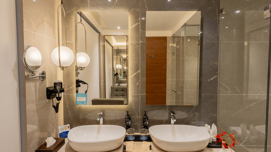 A close-up of a modern bathroom at an accommodation of Wyndham Garden featuring twin ceramic sinks set into a countertop, framed by 2 mirrors and wall.