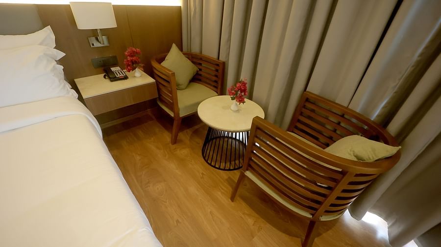 Cosy seating area with two wooden armchairs and a round table beside a bed with grey curtains at Wyndham Garden.