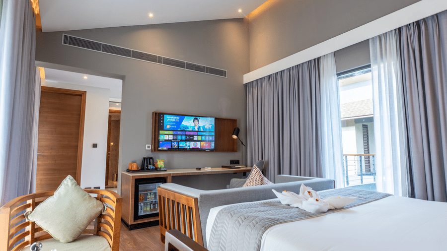 A Wyndham Garden bedroom with 2 separate beds, a mounted TV, and a window dressed with floor-length curtains.