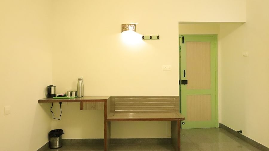 A room with a desk, chair, and a small table with a kettle.