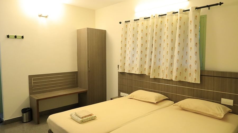 A bedroom at Wyt Hotels Transit Nest, Madurai featuring two single beds, bedside table, and a bench attached to it.
