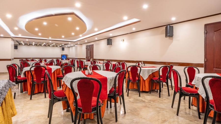 A spacious banquet hall at the Yashshree Jai Hotel & Banquet, featuring a setup with round tables, white cloths, and red chairs.