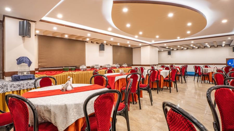 A modern banquet hall set up with red chairs and round tables at the Yashshree Jai Hotel & Banquet, Darjeeling.