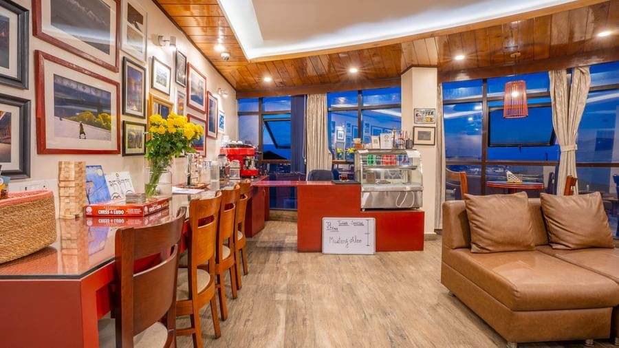 A comfortable lounge and cafe area with a sofa, bar stools, and framed photos at the Yashshree Jai Hotel & Banquet, Darjeeling.