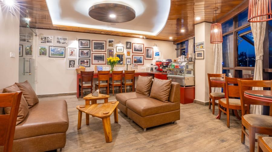 A modern lounge and cafe with brown sofas and bar seating at the Yashshree Jai Hotel & Banquet, Darjeeling.