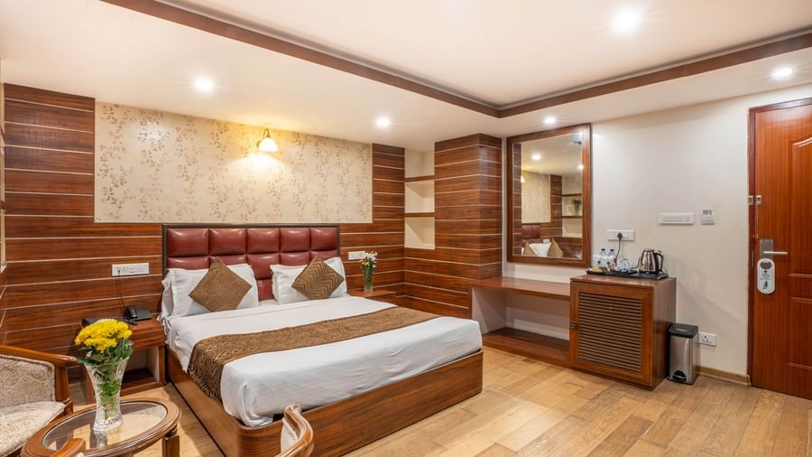 A stylish hotel room with a large bed, elegant wooden furnishings, and a cosy seating area at the Yashshree Jai Hotel & Banquet, Darjeeling.