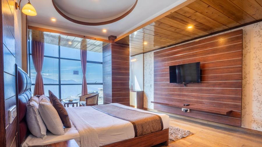 A well-appointed hotel room with a large bed, TV, and expansive windows at the Yashshree Jai Hotel & Banquet, Darjeeling.