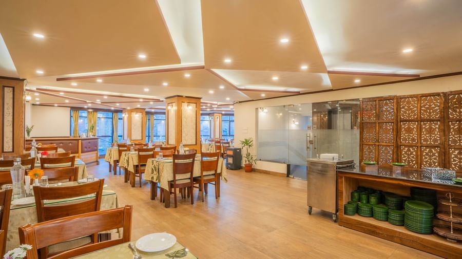 A bright and spacious hotel restaurant with tables, chairs, and a buffet counter at the Yashshree Jai Hotel & Banquet, Darjeeling.