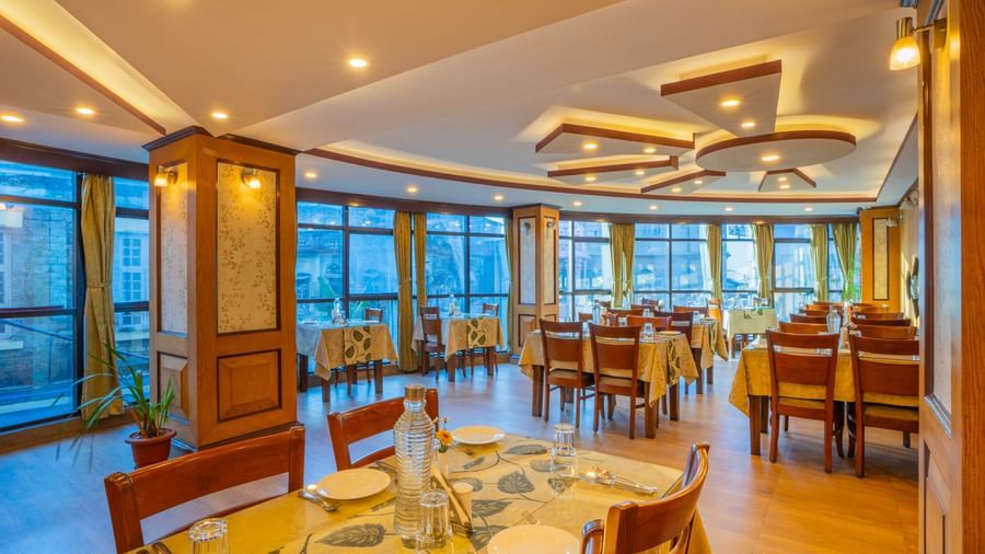 A brightly lit restaurant at the Yashshree Jai Hotel & Banquet, Darjeeling, with tables, chairs, and large windows.