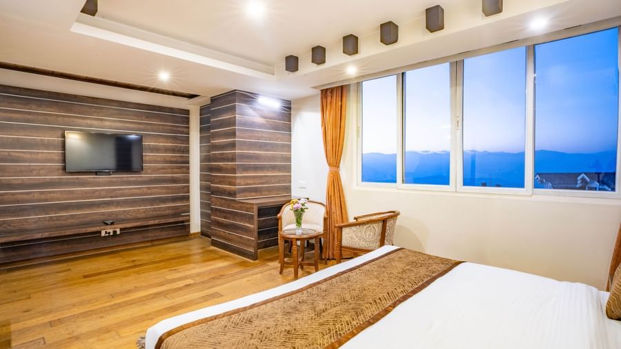 A spacious and well-lit hotel room with a large bed, seating area, and a flat-screen TV at the Yashshree Jai Hotel & Banquet, Darjeeling.