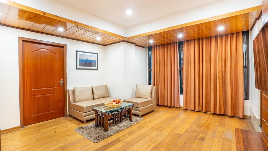 A hotel suite's living room with comfortable sofas, a wooden coffee table, and curtains at the Yashshree Jai Hotel & Banquet, Darjeeling.