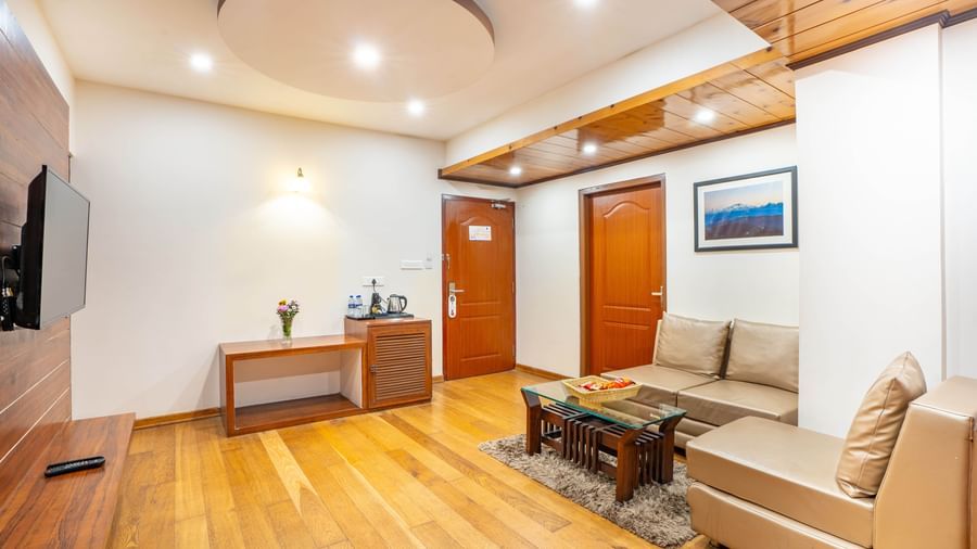 A spacious hotel suite living room with a sofa, coffee table, and flat-screen TV at the Yashshree Jai Hotel & Banquet, Darjeeling.
