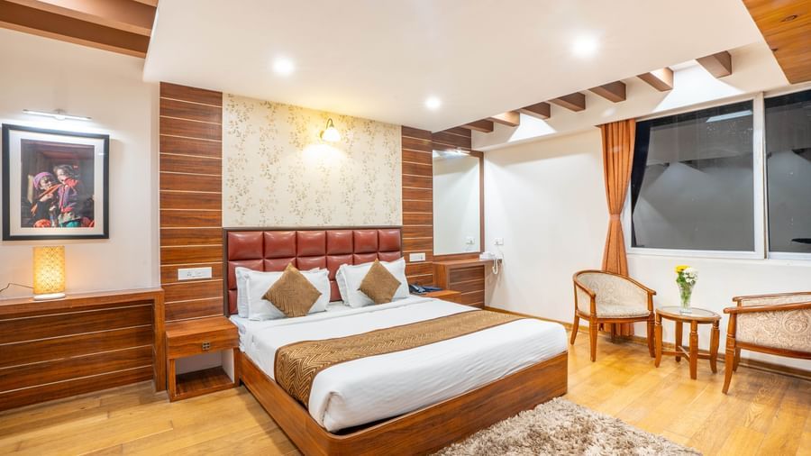 A comfortable hotel bedroom with a large bed, seating area, and a view of the street from the window at the Yashshree Jai Hotel & Banquet, Darjeeling.