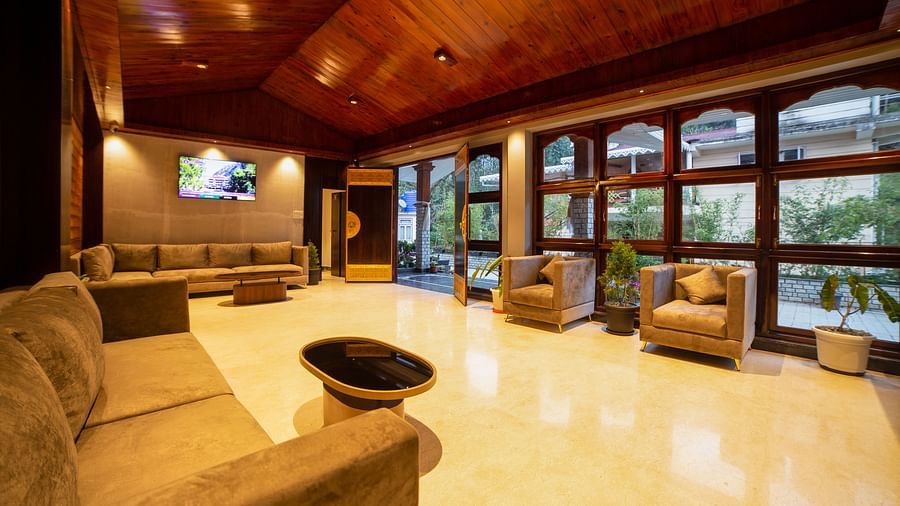 Elegant hotel lobby with a polished floor, cosy sofas and armchairs, wooden vaulted ceiling, large windows providing natural light, and a television mounted on the wall - Yashshree Pelling Chekhim Retreat.