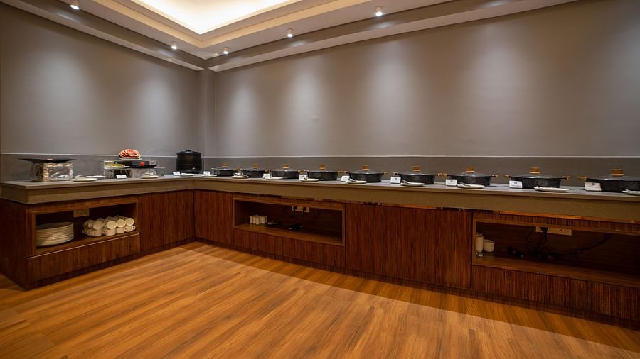 Contemporary buffet area featuring U-shaped counters, wooden flooring, grey walls, recessed ceiling lighting, and an assortment of food and beverages arranged on the counters - Yashshree Pelling Chekhim Retreat.