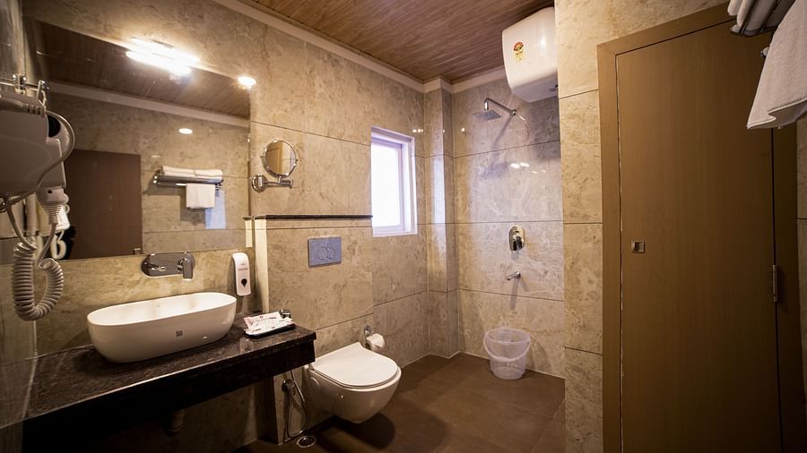 Spacious modern bathroom featuring a wall-mounted sink, a floating toilet, an open shower area with a handheld showerhead, beige tiled walls, a wooden ceiling, and contemporary lighting - Yashshree Pelling Chekhim Retreat.